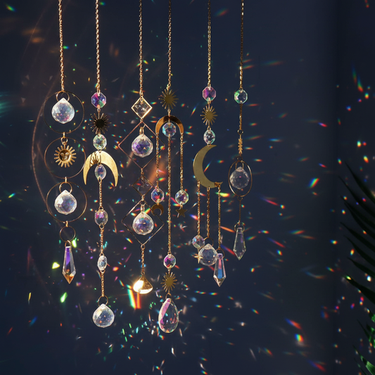 Multiple gold celestial crystal suncatchers with moon and star charms casting rainbow light against a dark background